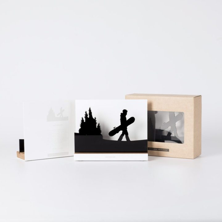 Figure "Snowboard · Board in hand among the pines" next to its sleeve and its gift box